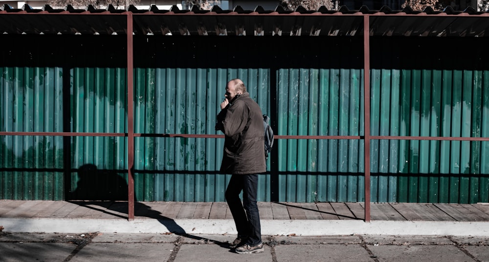 homme en veste noire debout près de la porte en métal vert pendant la journée
