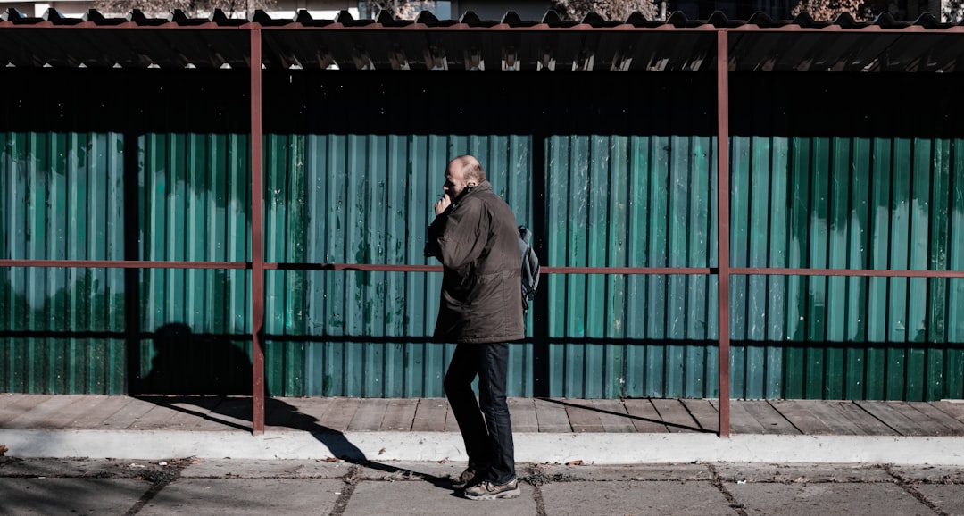 man in black jacket standing near green metal gate during daytime