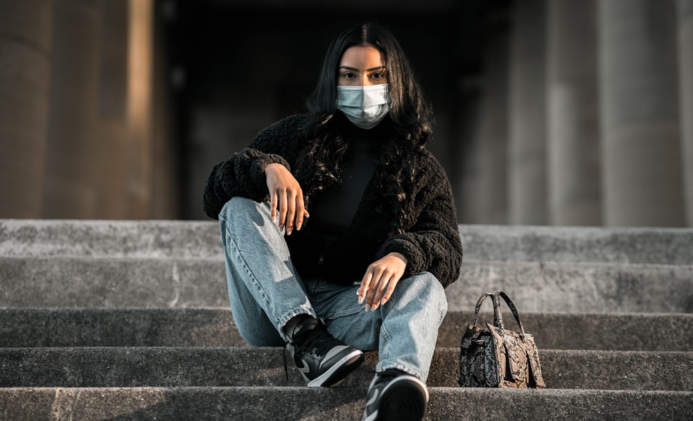 woman in black sweater and blue denim jeans sitting on concrete bench
