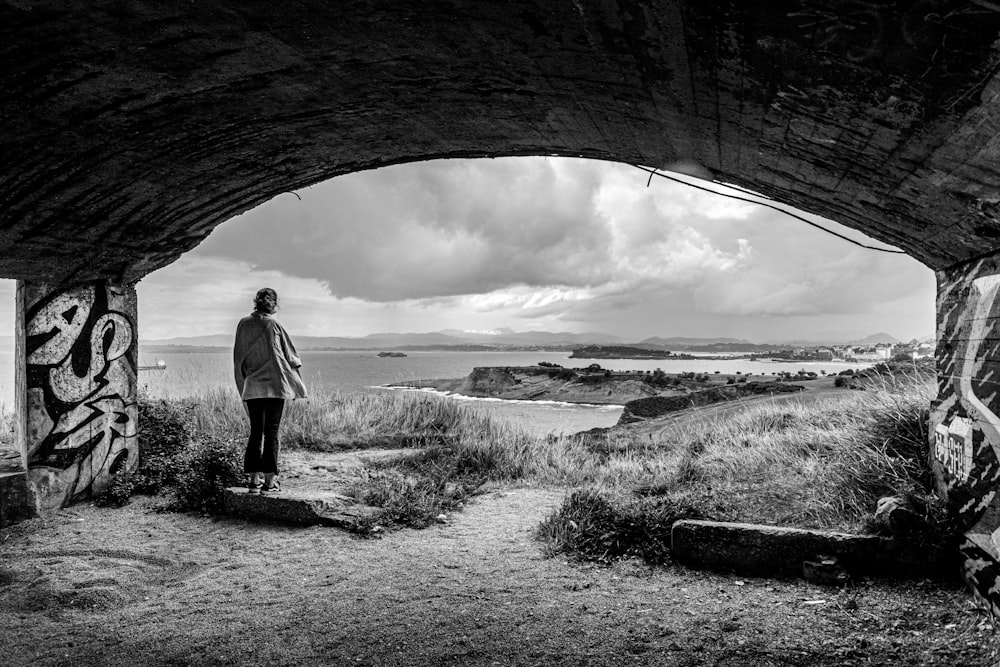 grayscale photo of man in white long sleeve shirt standing on rock formation