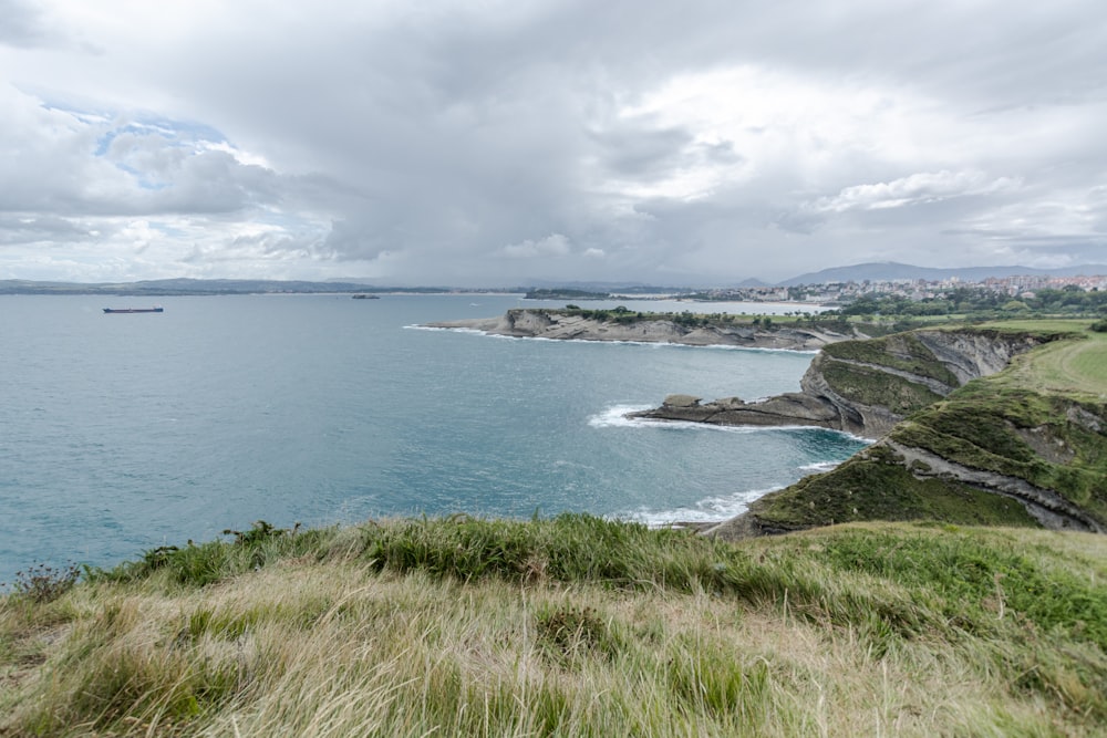 campo de hierba verde cerca del cuerpo de agua bajo nubes blancas durante el día