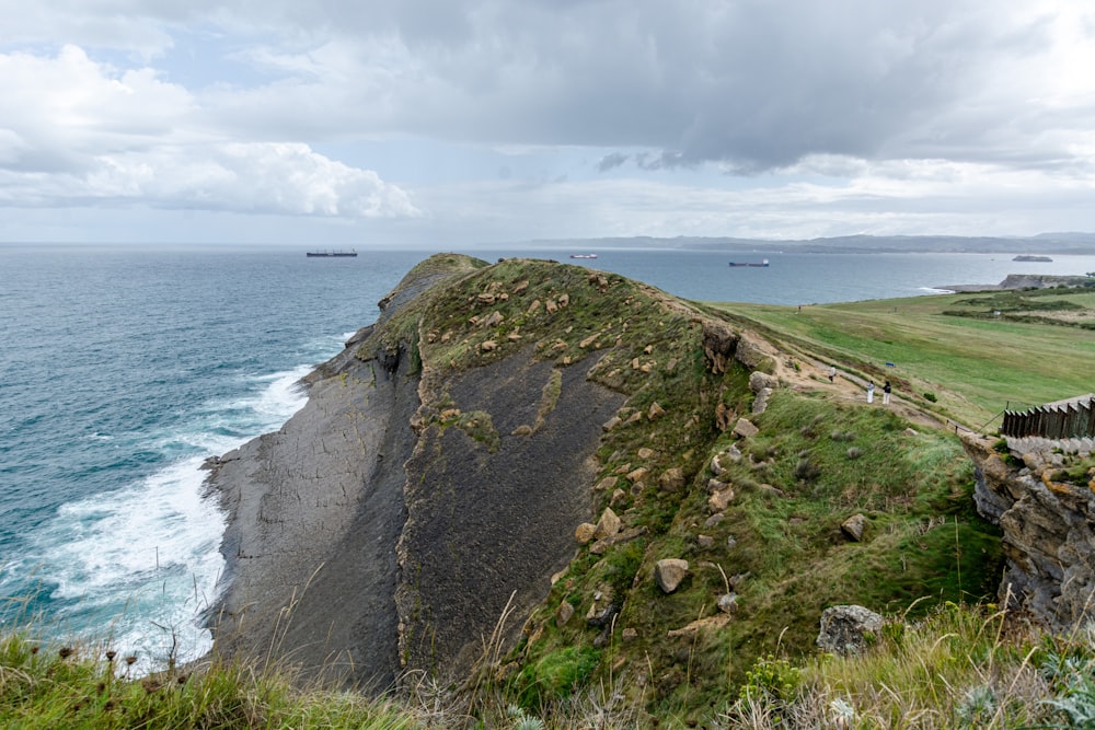 green grass covered mountain by the sea under white clouds during daytime