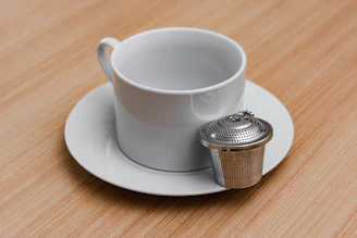 Close-up of a stainless steel tea infuser resting on a white ceramic cup with steam rising.