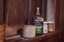 A wooden shelf holds a bottle of 'Liquid Hide Glue', a roll of twine, and two jars. One jar appears to contain small grains or seeds, and the other holds a white substance. The setting suggests a rustic or vintage atmosphere.