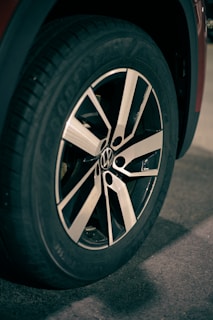 A close-up view of a car wheel with a modern alloy rim, featuring a distinct pattern with black and silver spokes. The tire appears to be a standard road tire with visible tread and branding.