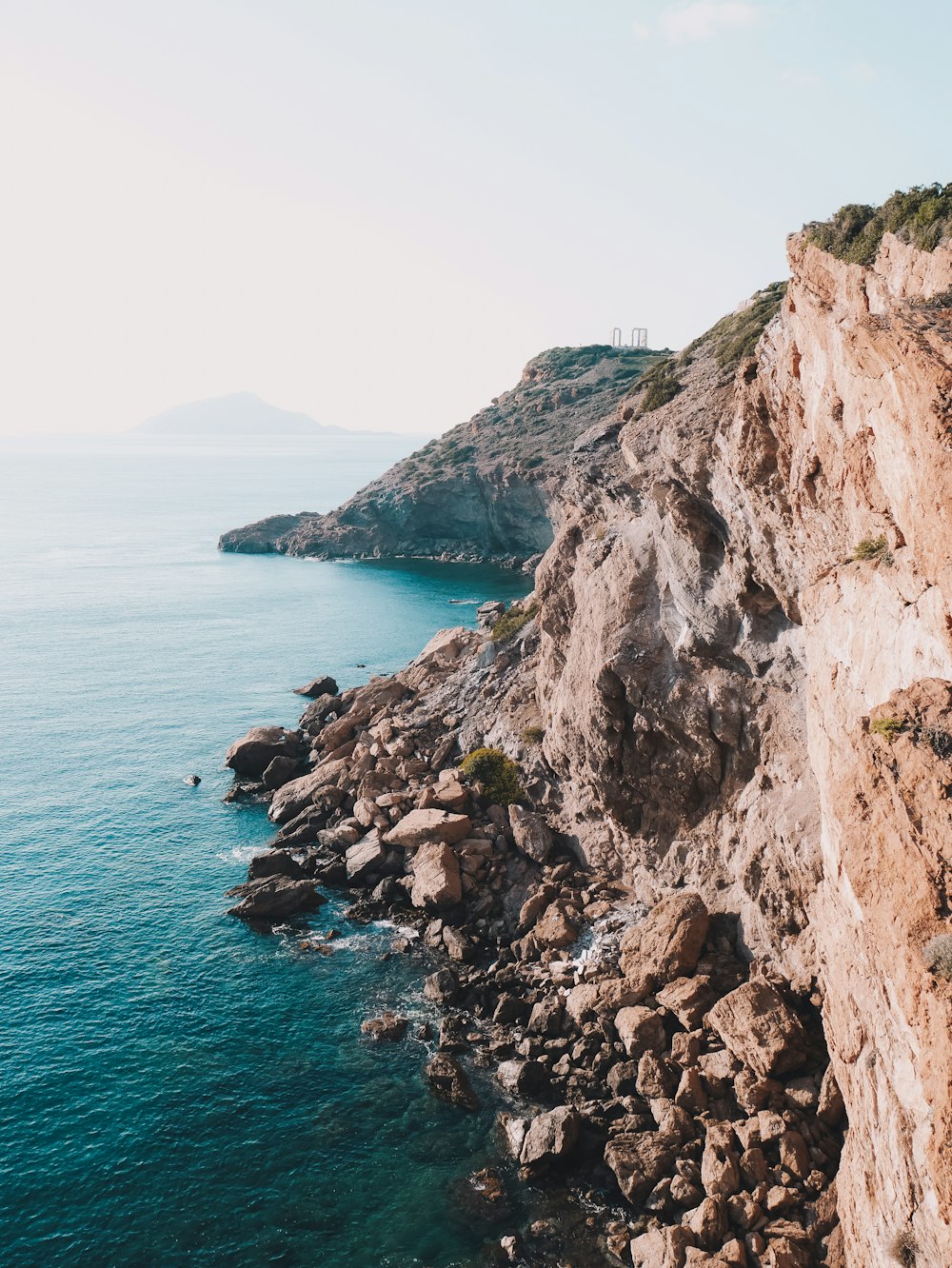 brown rocky mountain beside blue sea under blue sky during daytime