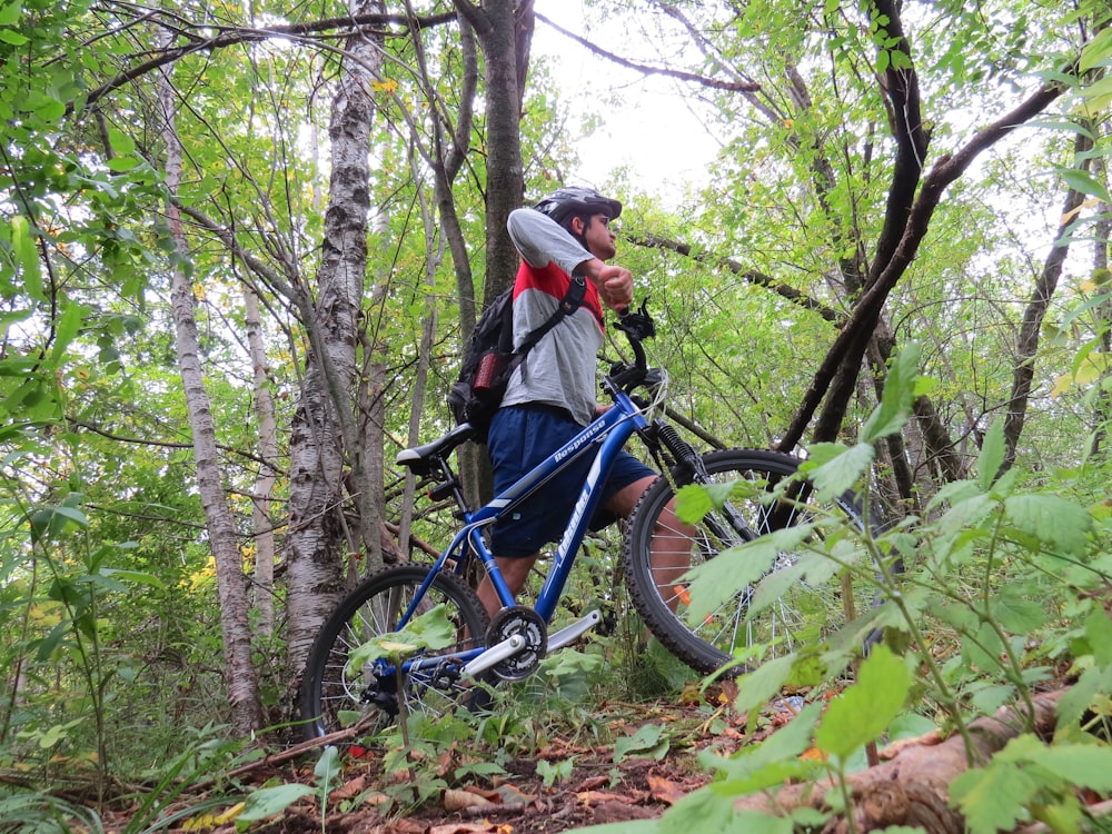 man in gray jacket riding blue mountain bike on forest during daytime