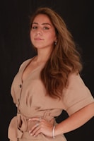 A soft-toned photo of a model wearing a flowing beige dress paired with minimalist gold jewelry.