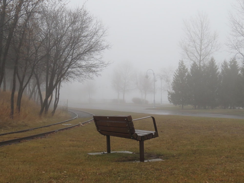 brown wooden bench on green grass field surrounded by fog during daytime
