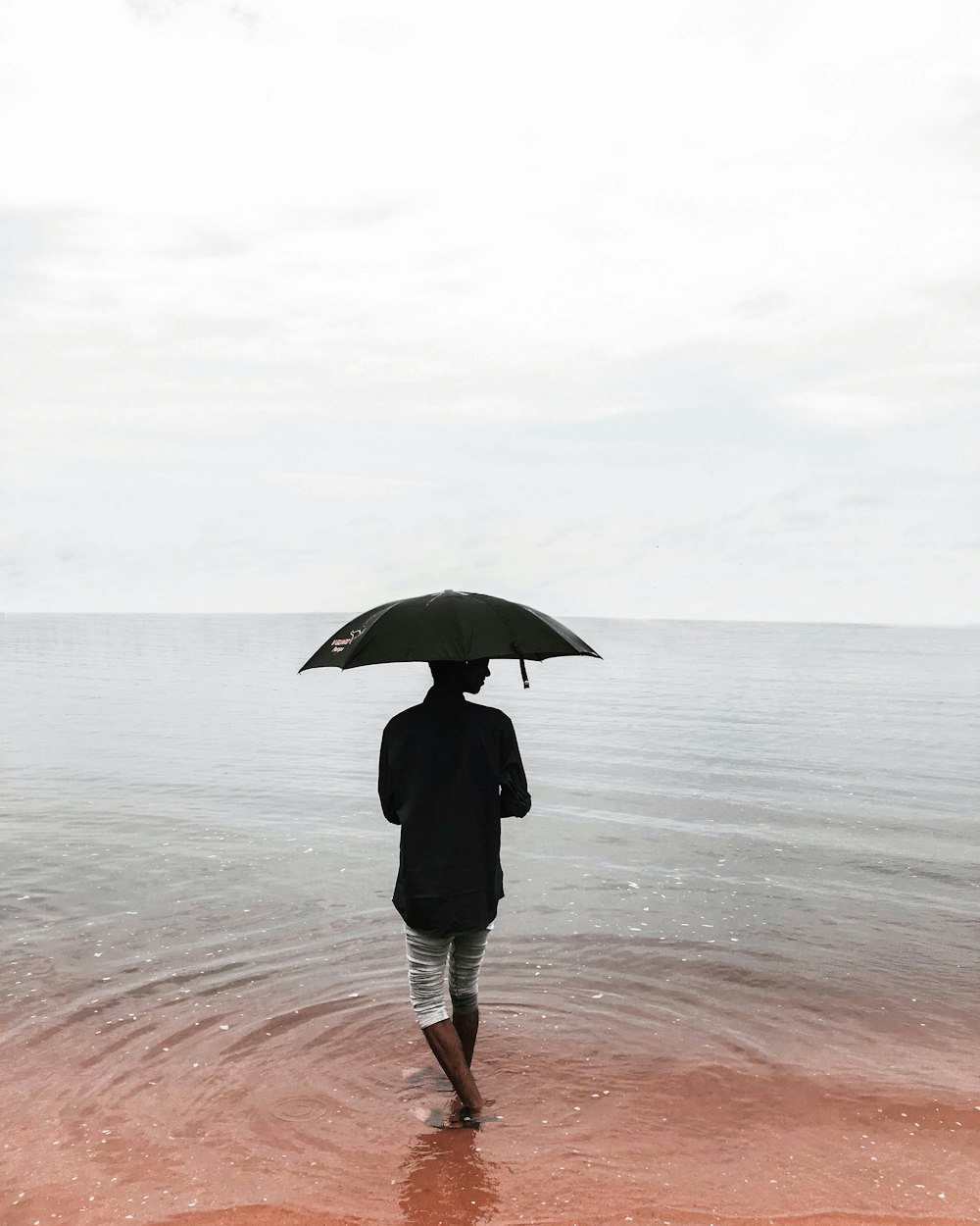 person in black coat holding umbrella standing on beach during daytime