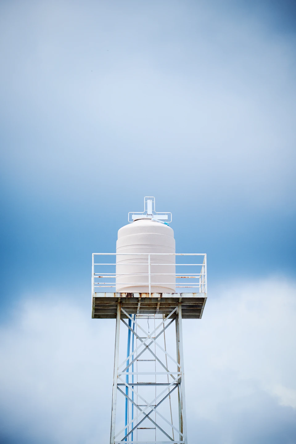 Large white water tower stands tall against clear blue sky with fluffy white clouds