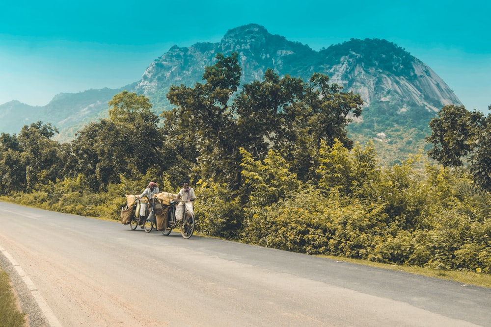 people riding horses on road near green trees and mountain during daytime