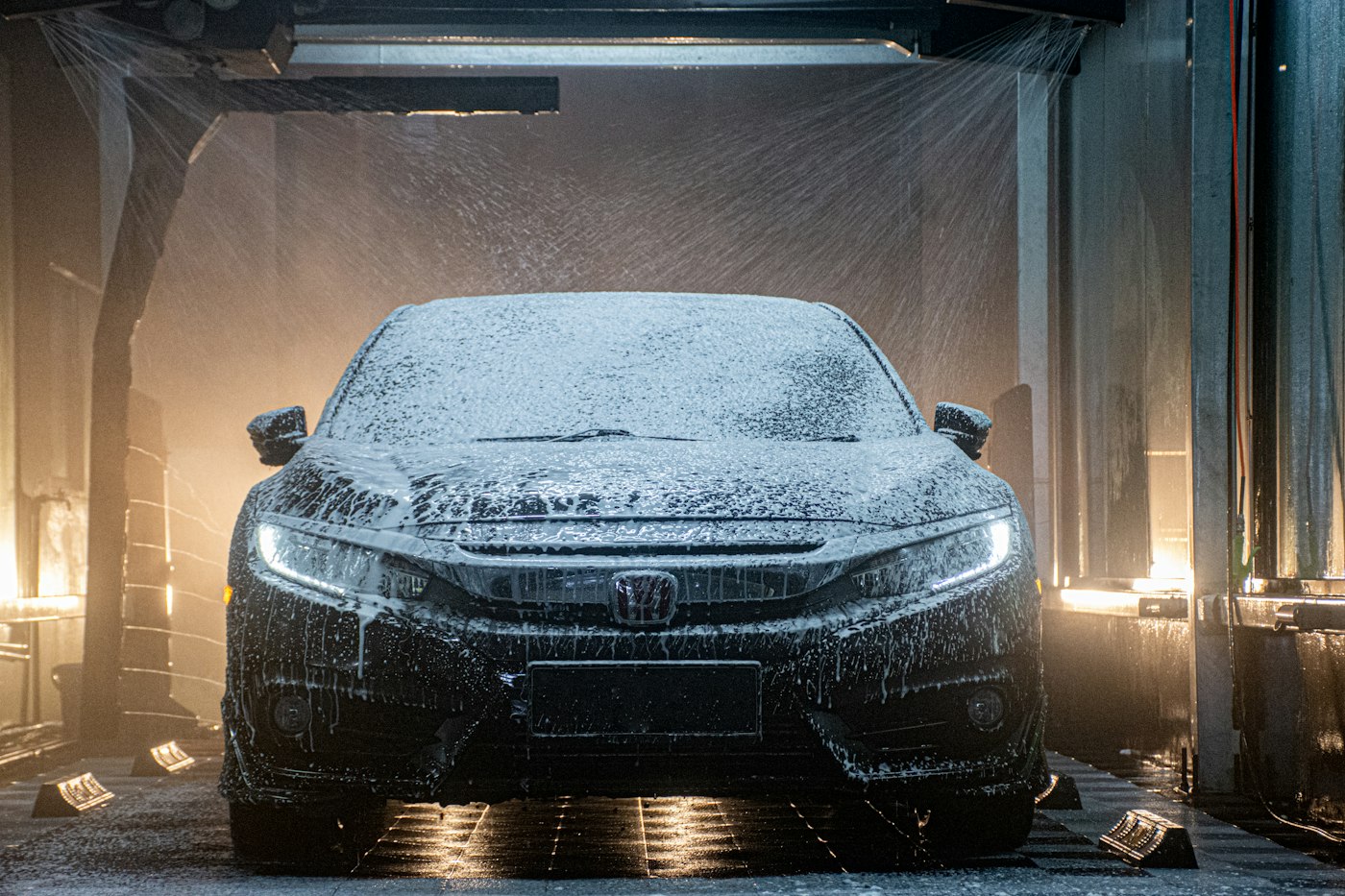 Foam-covered car passing through an automatic car wash tunnel at night with dramatic lighting