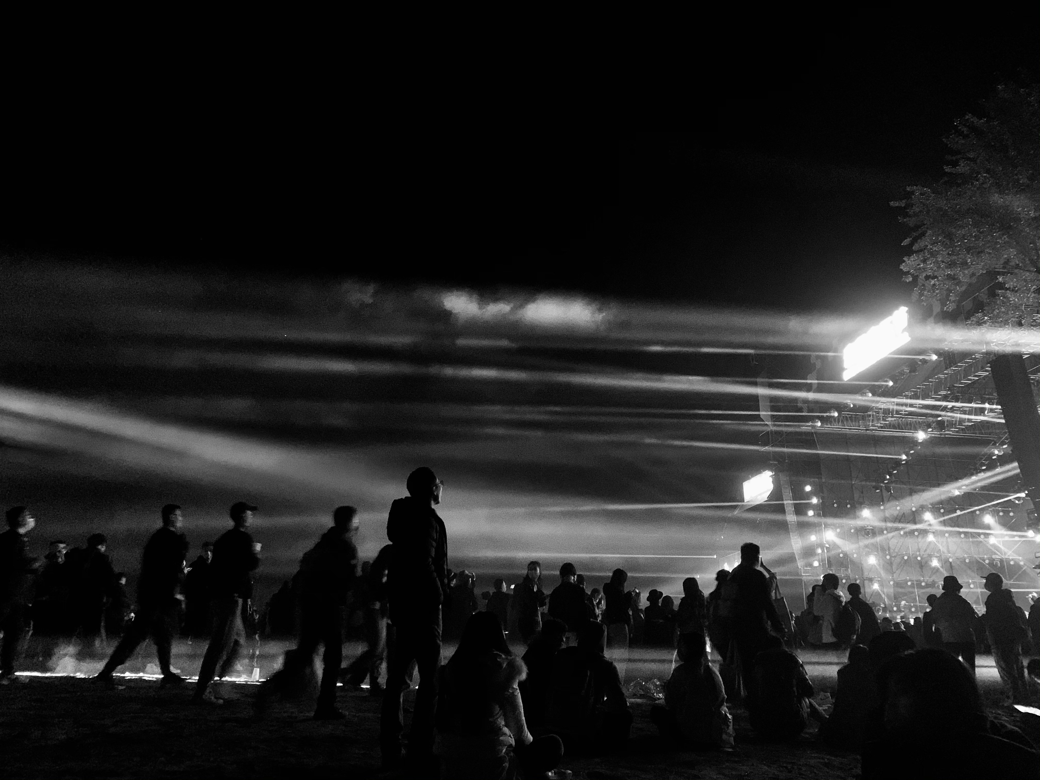 Concert stage with dramatic lighting, colorful spotlights, smoke effects, large crowd in silhouette