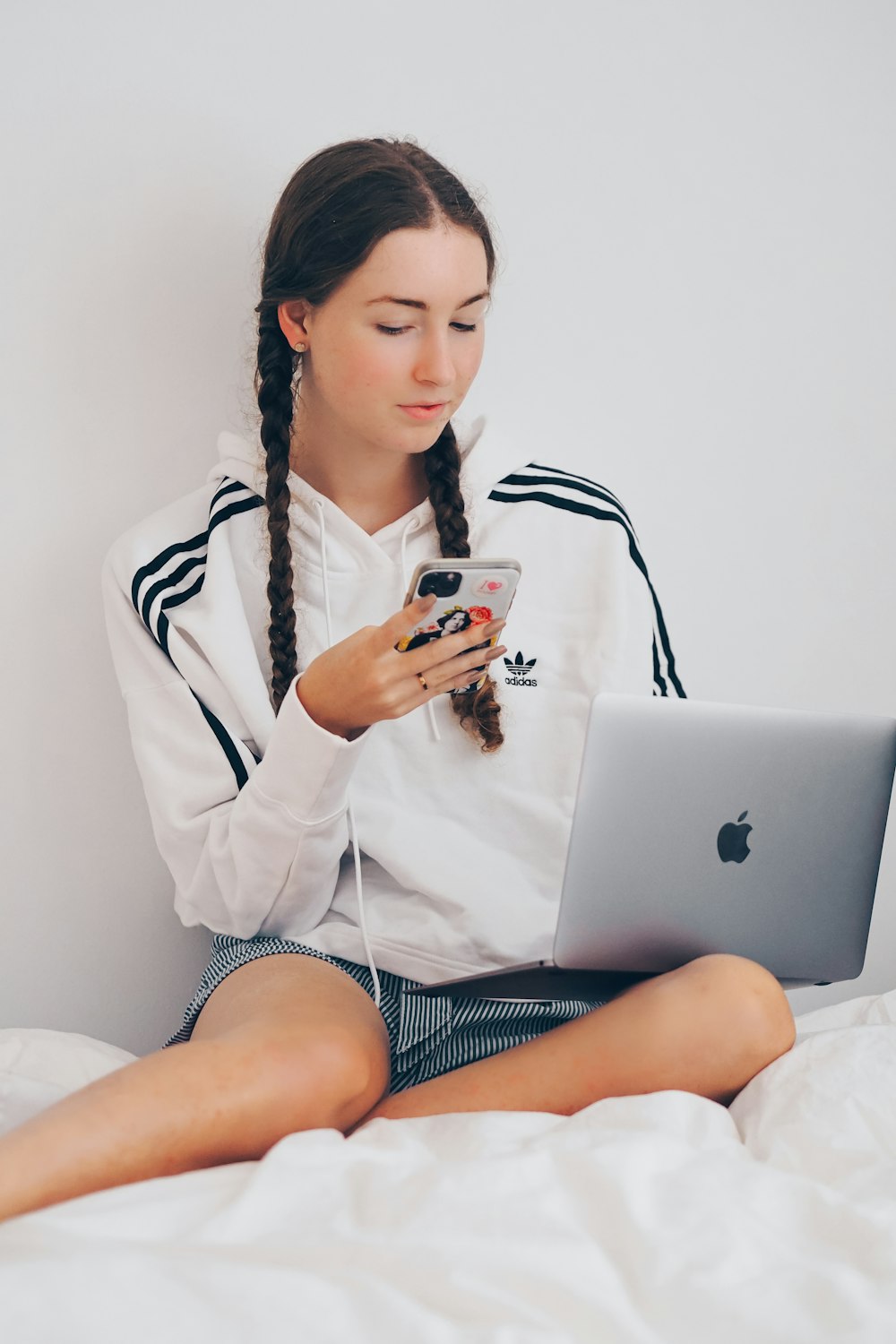 woman in white coat sitting on bed using silver macbook