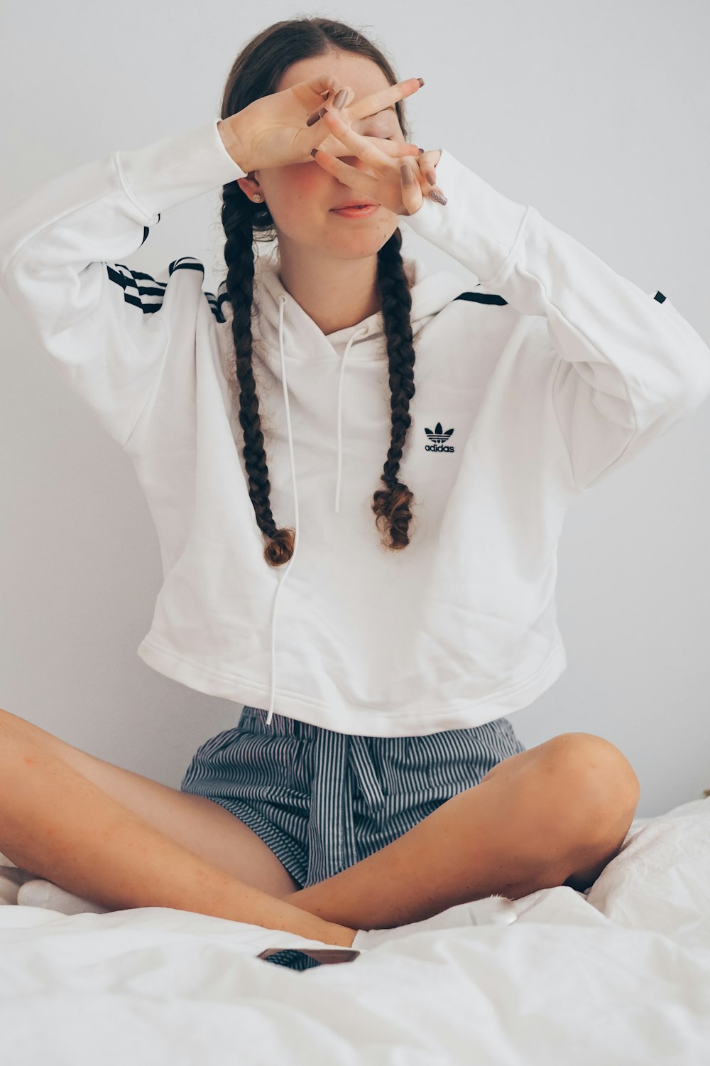 woman in white shirt and black and white striped shorts sitting on white bed