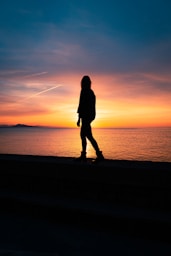 silhouette of woman standing on seashore during sunset