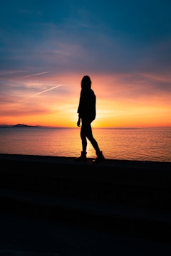 silhouette of woman standing on seashore during sunset