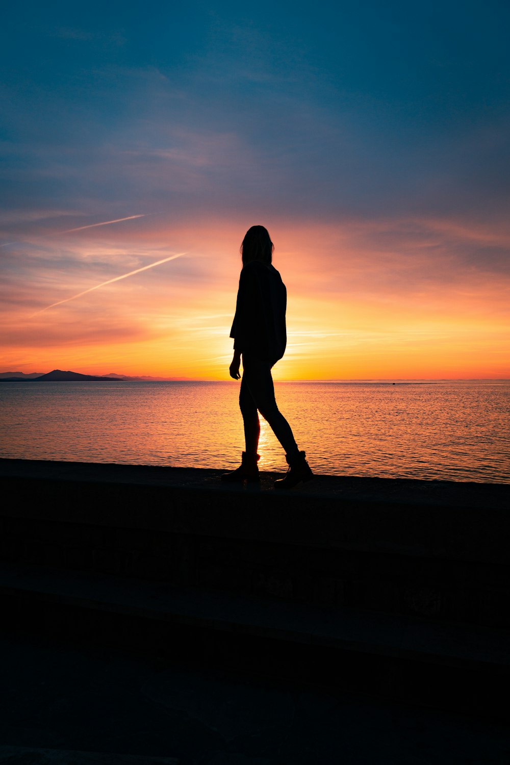 silhouette of woman standing on seashore during sunset