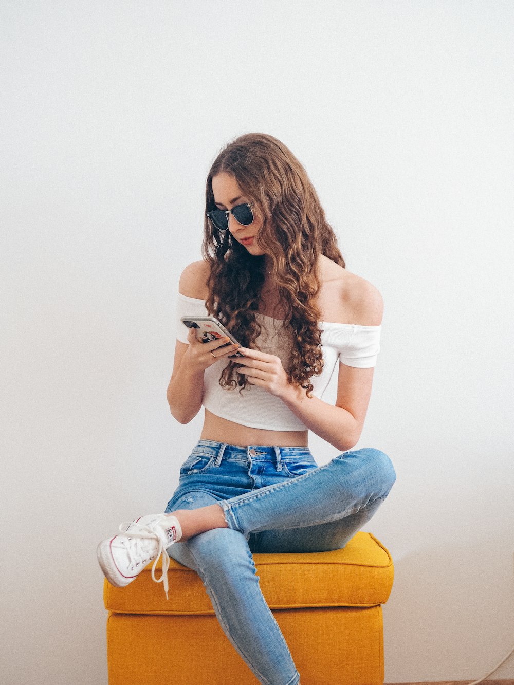 woman in white tank top and blue denim jeans sitting on orange chair