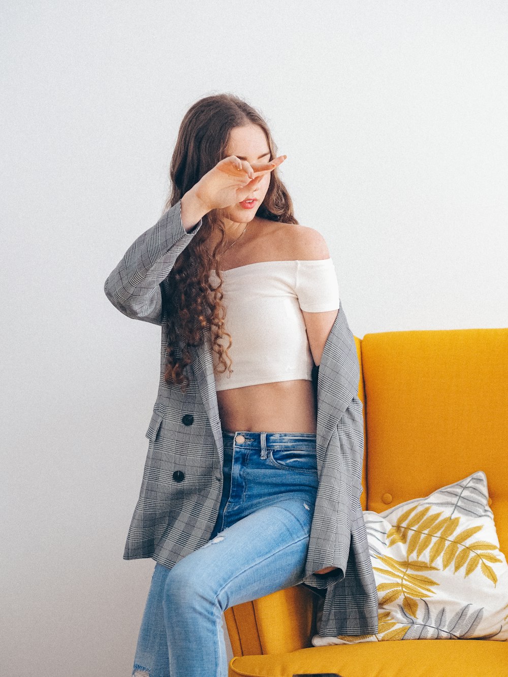 woman in gray coat and blue denim jeans sitting on yellow sofa