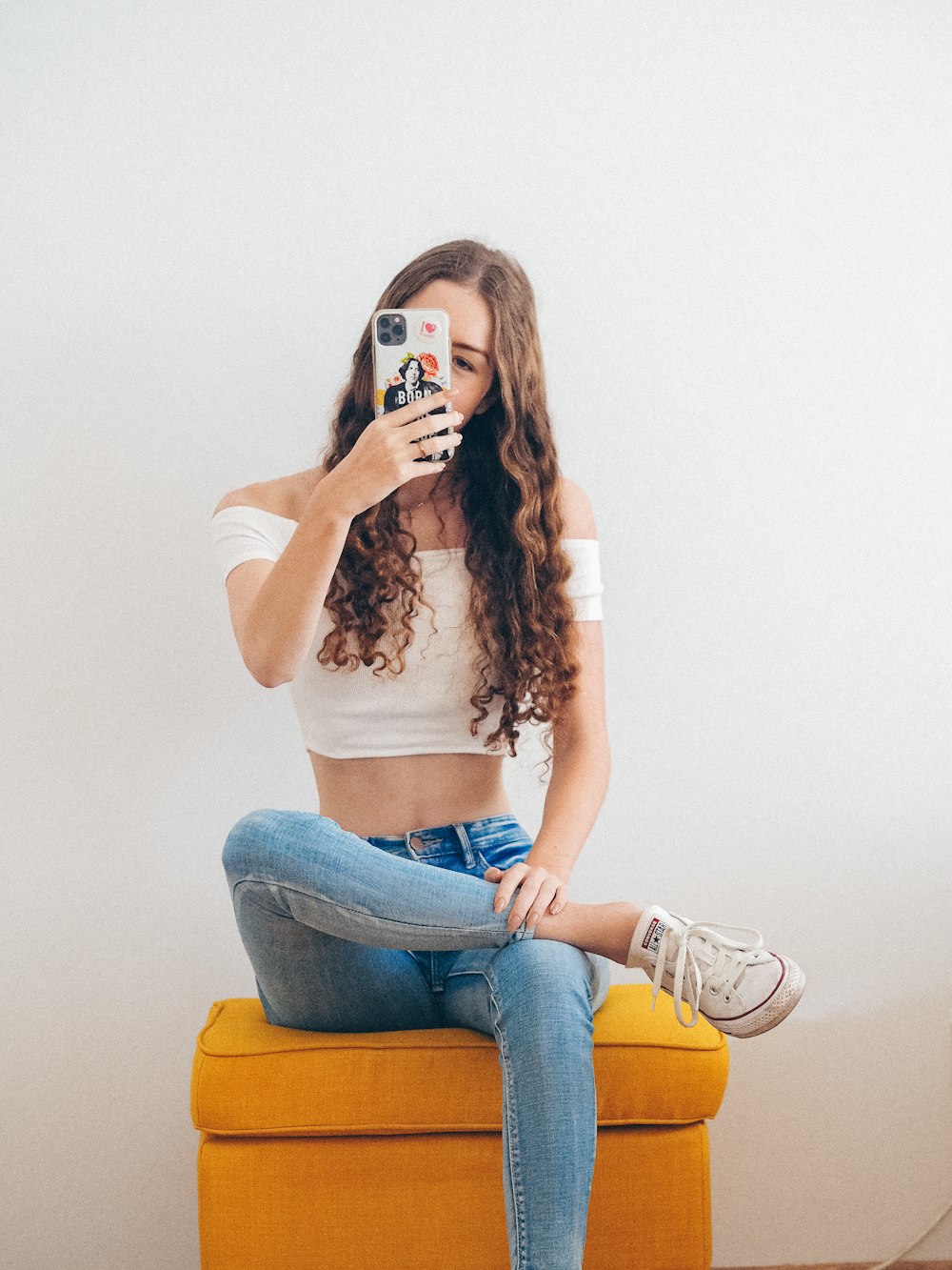 Frau in weißem Crop-Top und blauer Jeans sitzt auf braunem Holzsitz