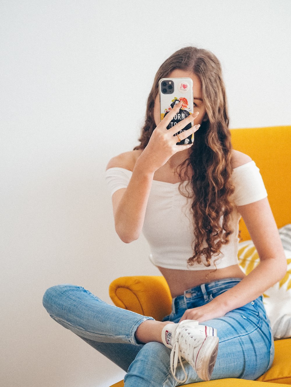 woman in white tank top and blue denim jeans sitting on yellow chair