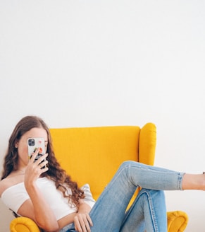 woman in white tank top and blue denim jeans sitting on yellow sofa