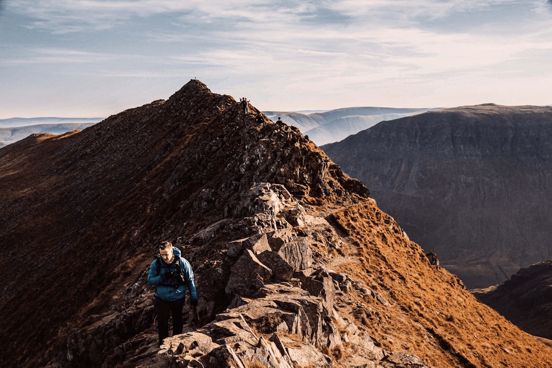 man in blue jacket and blue denim jeans standing on brown rock mountain during daytime