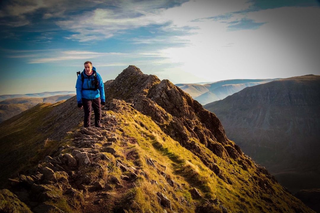 man in blue jacket and black pants standing on brown rocky mountain during daytime