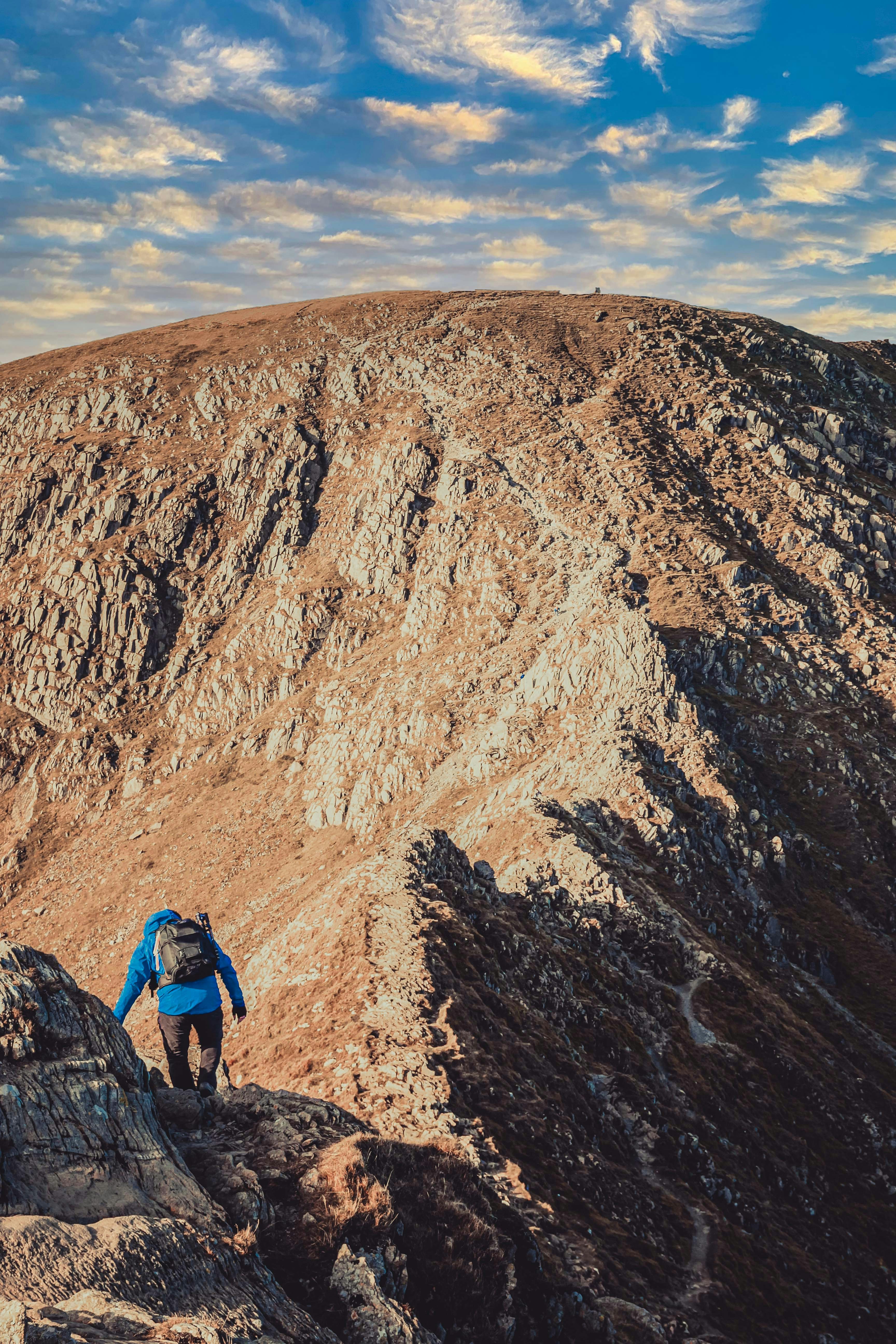 man in blue jacket and blue backpack standing on brown rocky mountain during daytime