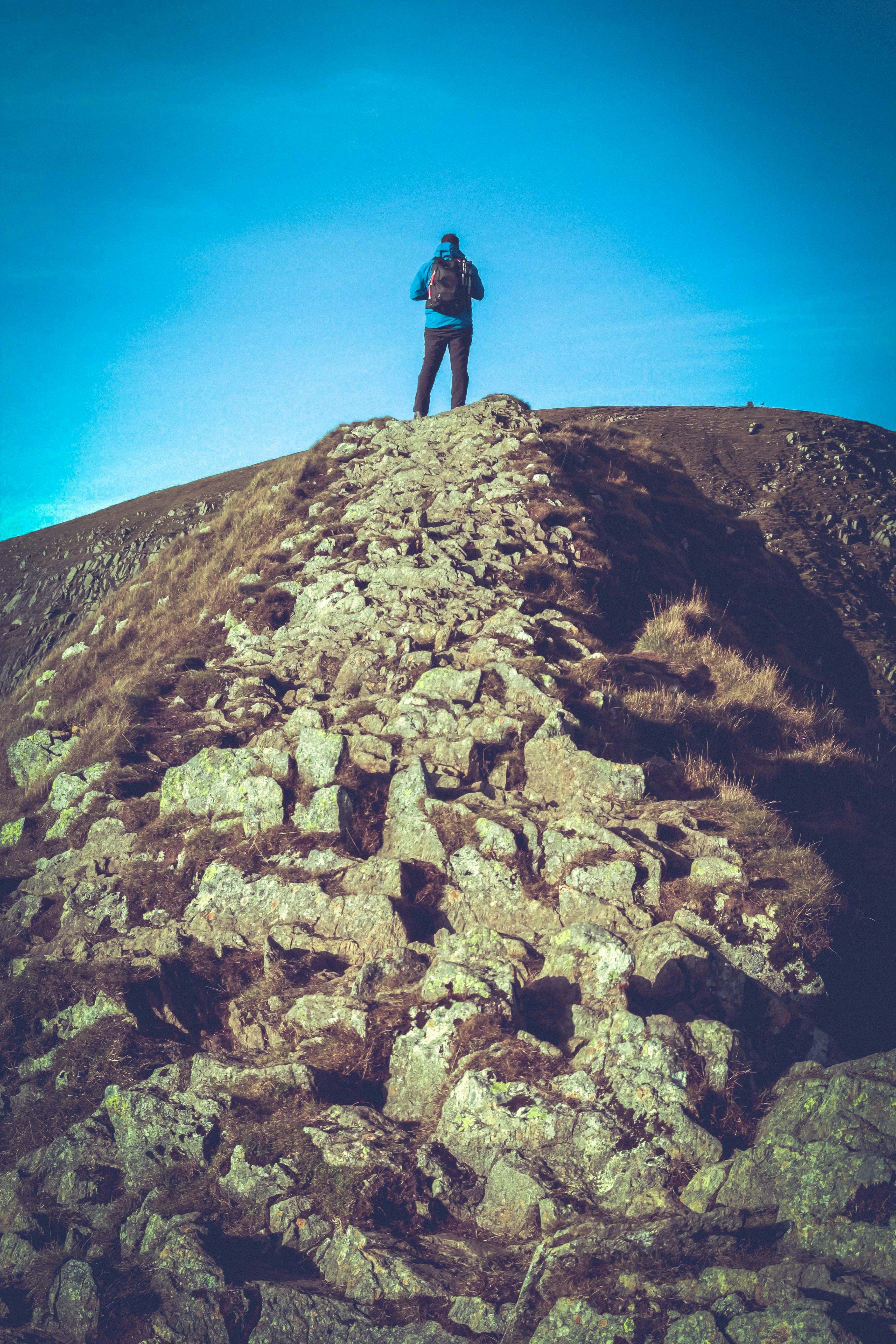 person in black jacket standing on brown rock mountain during daytime