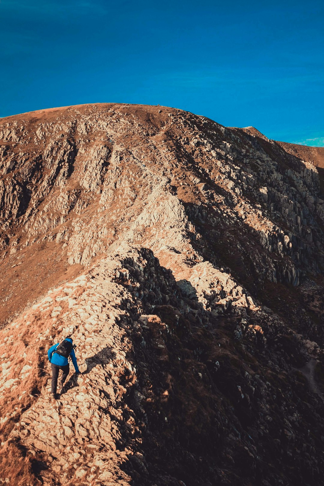 man in blue jacket and blue backpack walking on rocky mountain during daytime