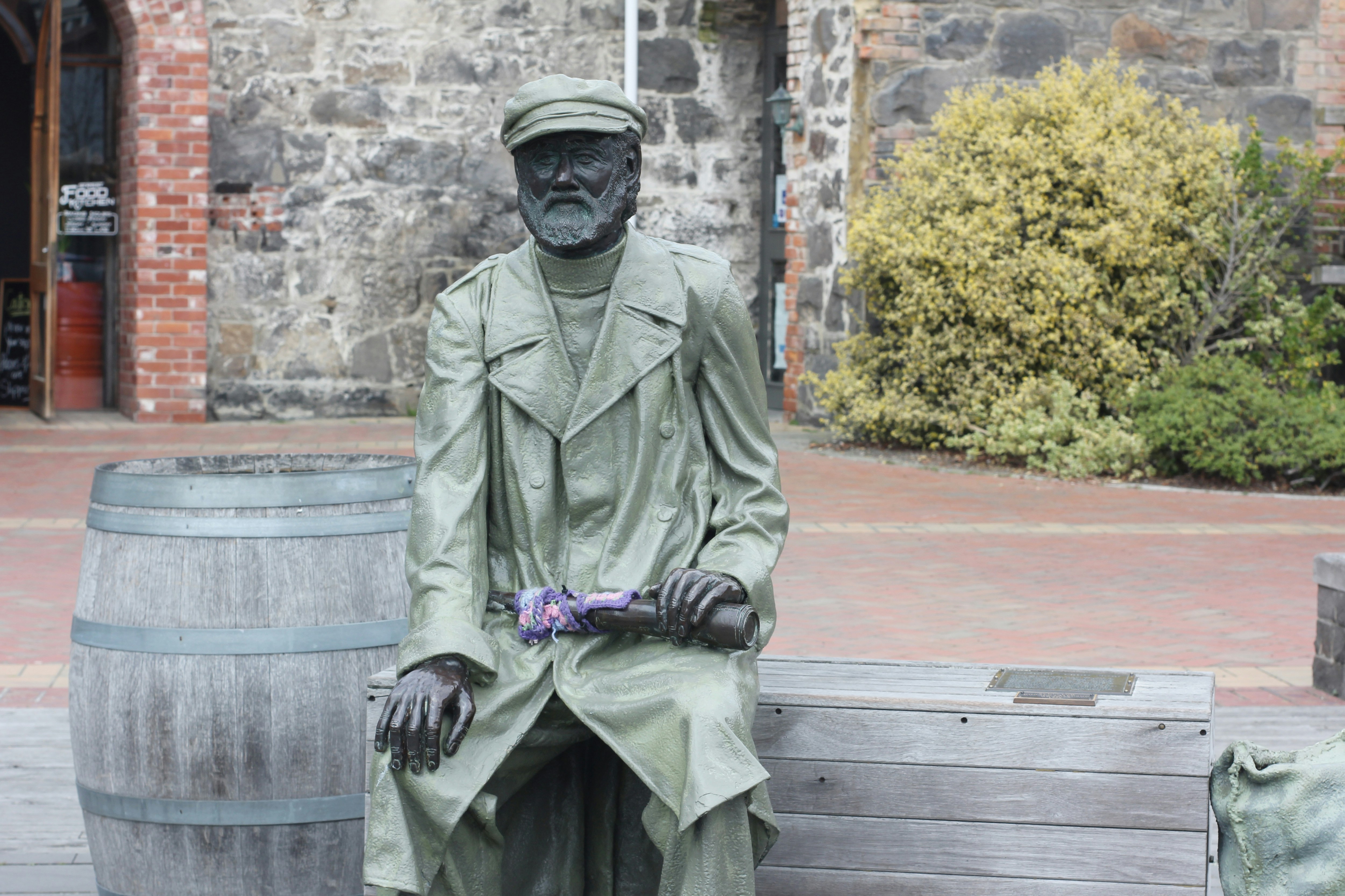 Mann in schwarzer Lederjacke sitzt auf Bank Statue