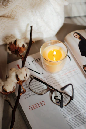 A cozy scene with a hand-poured candle glowing softly beside a book and dried flowers.