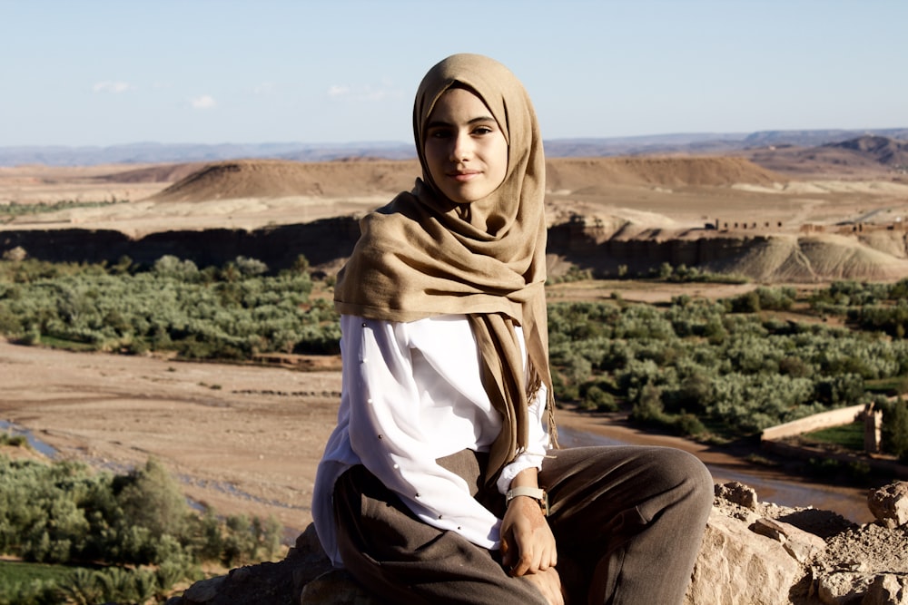 Frau im braunen Hijab sitzt auf braunem Felsen