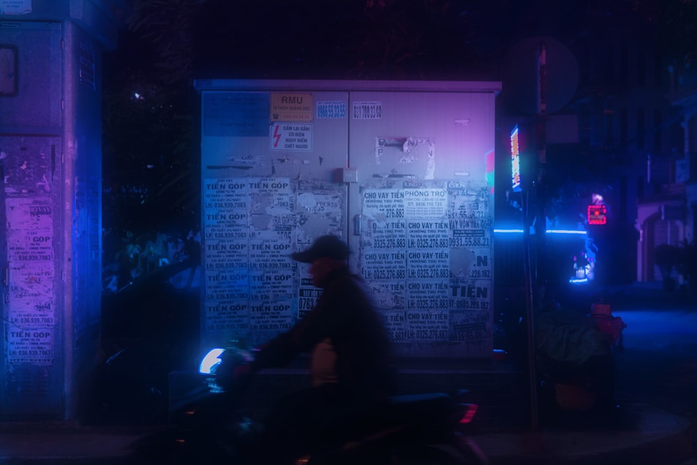 man in black jacket standing near white and blue poster during nighttime