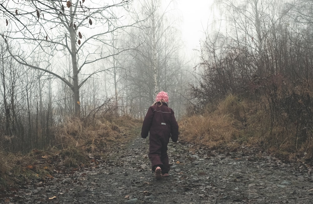 woman in black jacket standing on pathway between bare trees