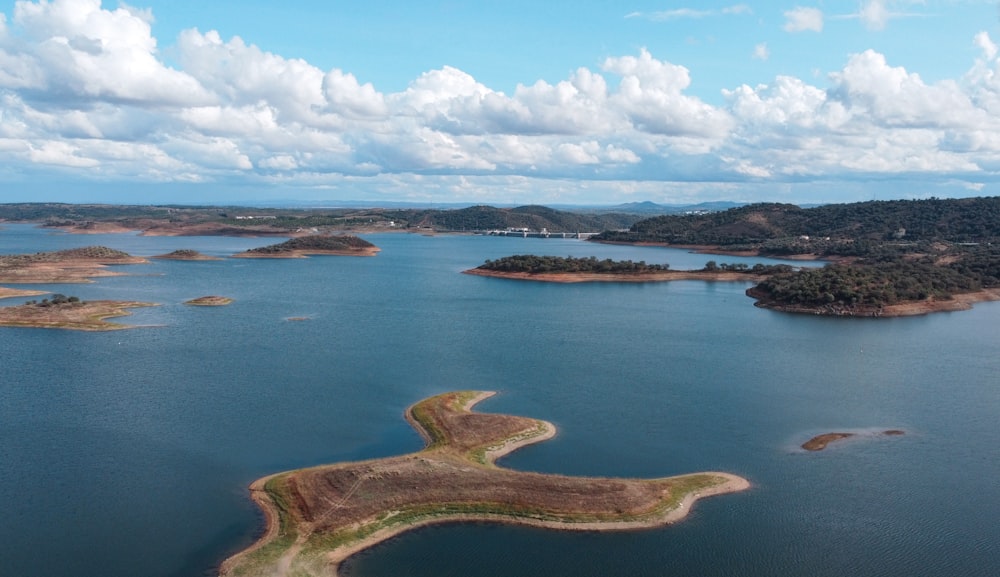 body of water near brown field under white clouds and blue sky during daytime