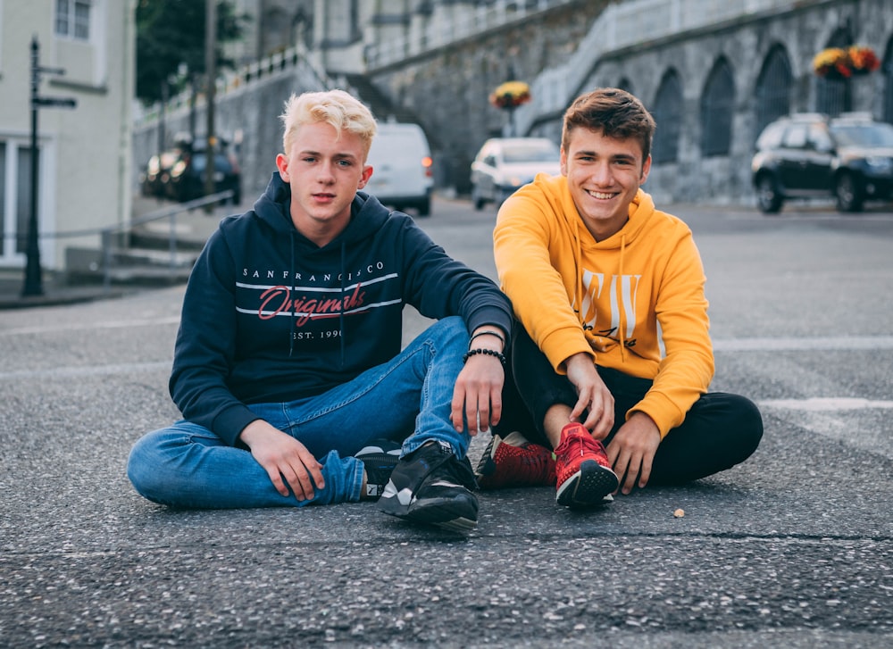 2 boys sitting on gray concrete floor during daytime