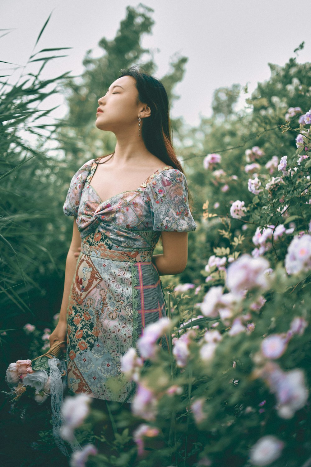 Mujer en vestido floral rojo y blanco de pie cerca de flores blancas durante el día