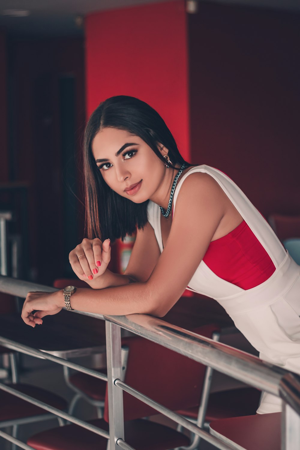 woman in red and white tank top and white pants sitting on brown wooden chair