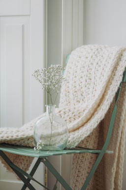 A cozy crochet blanket draped over a chair next to a small vase of fresh flowers.