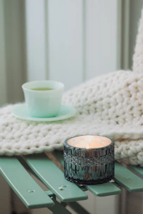 A cozy lifestyle scene with soft cream and sage green accents, featuring a warm throw blanket and a steaming cup of tea on a wooden table.