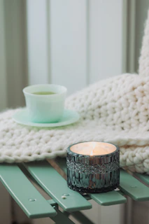 Cozy flat lay of a calming tea cup, a notebook, and a muted sage green candle on a cream background.