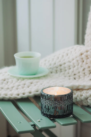 Cozy flat lay of a calming tea cup, a notebook, and a muted sage green candle on a cream background.