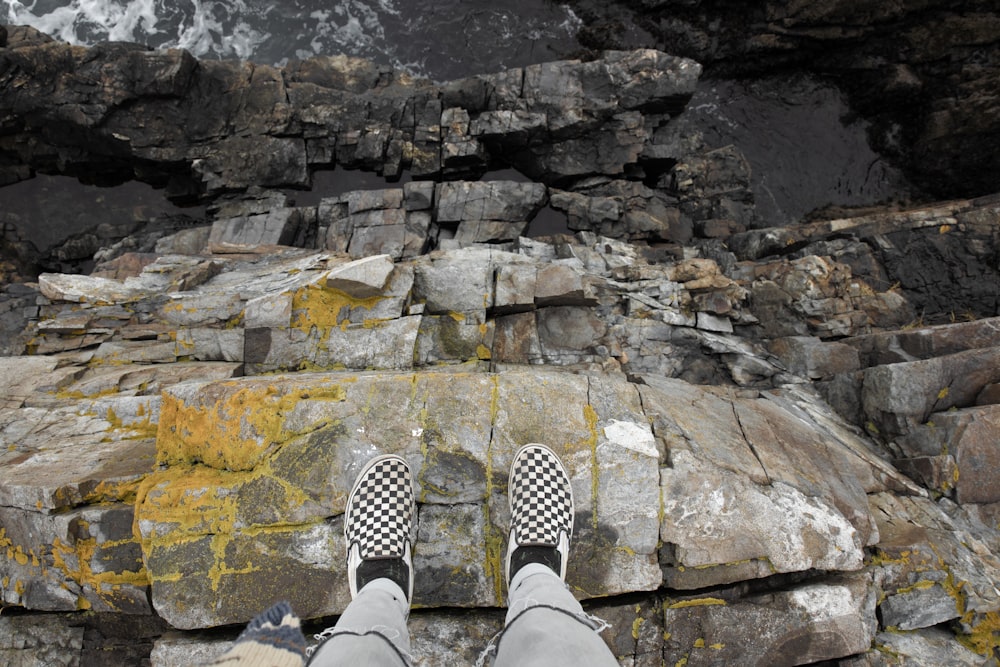 person in white pants and black and white checkered sneakers standing on rocky ground during daytime