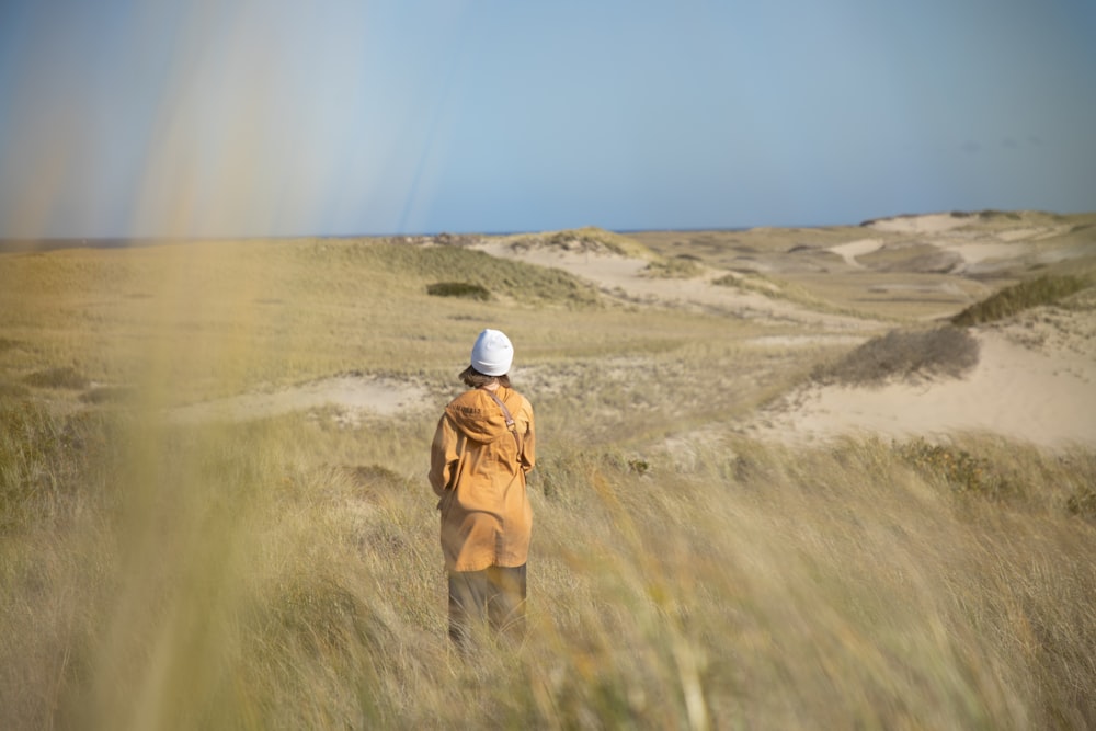 person in brown jacket and white cap walking on brown field during daytime