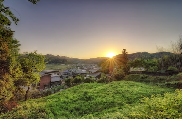 A serene sunrise over a quiet Southeast Asian village with lush greenery and traditional houses.