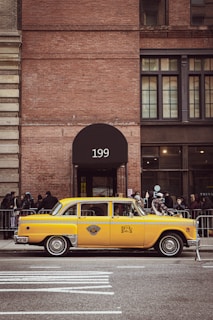 A friendly taxi driver standing next to a yellow taxi car in a city street.